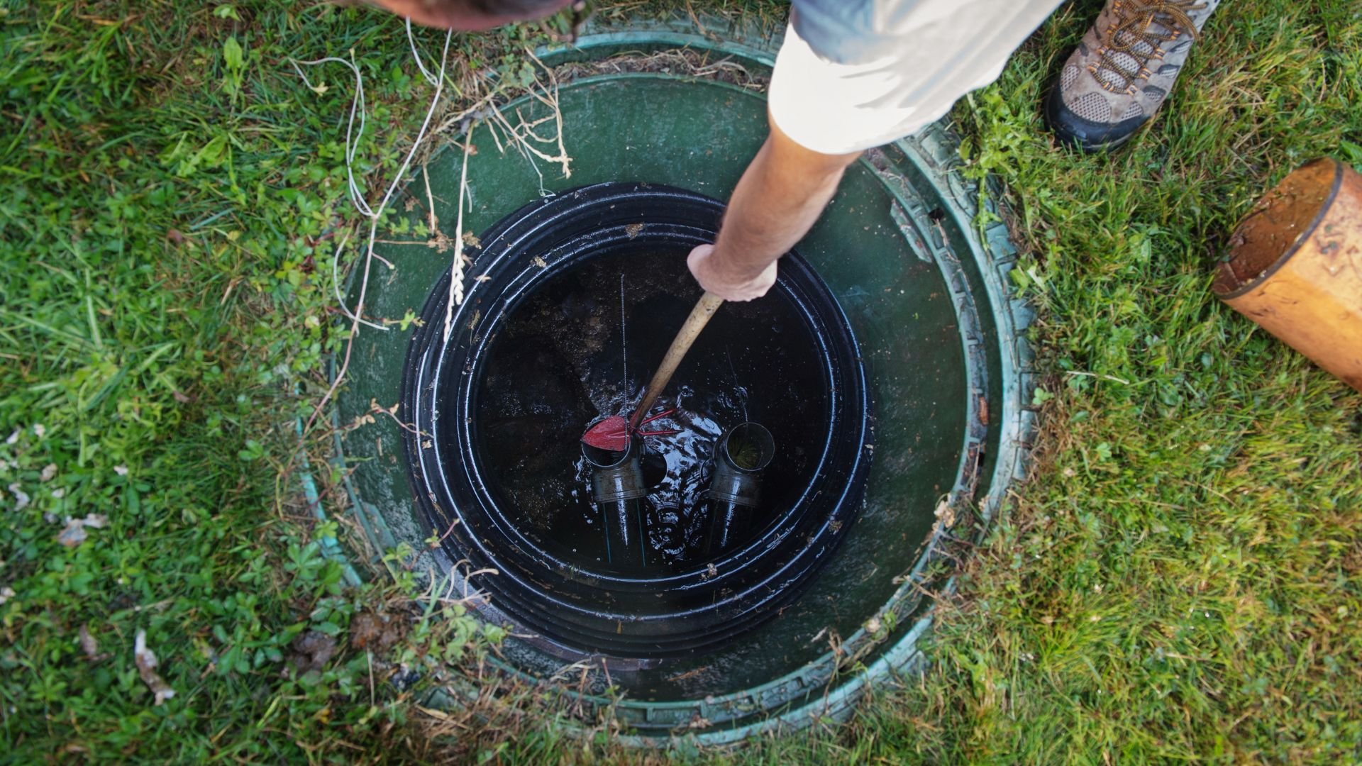 Hand stirring dark liquid in a green outdoor water tank or well