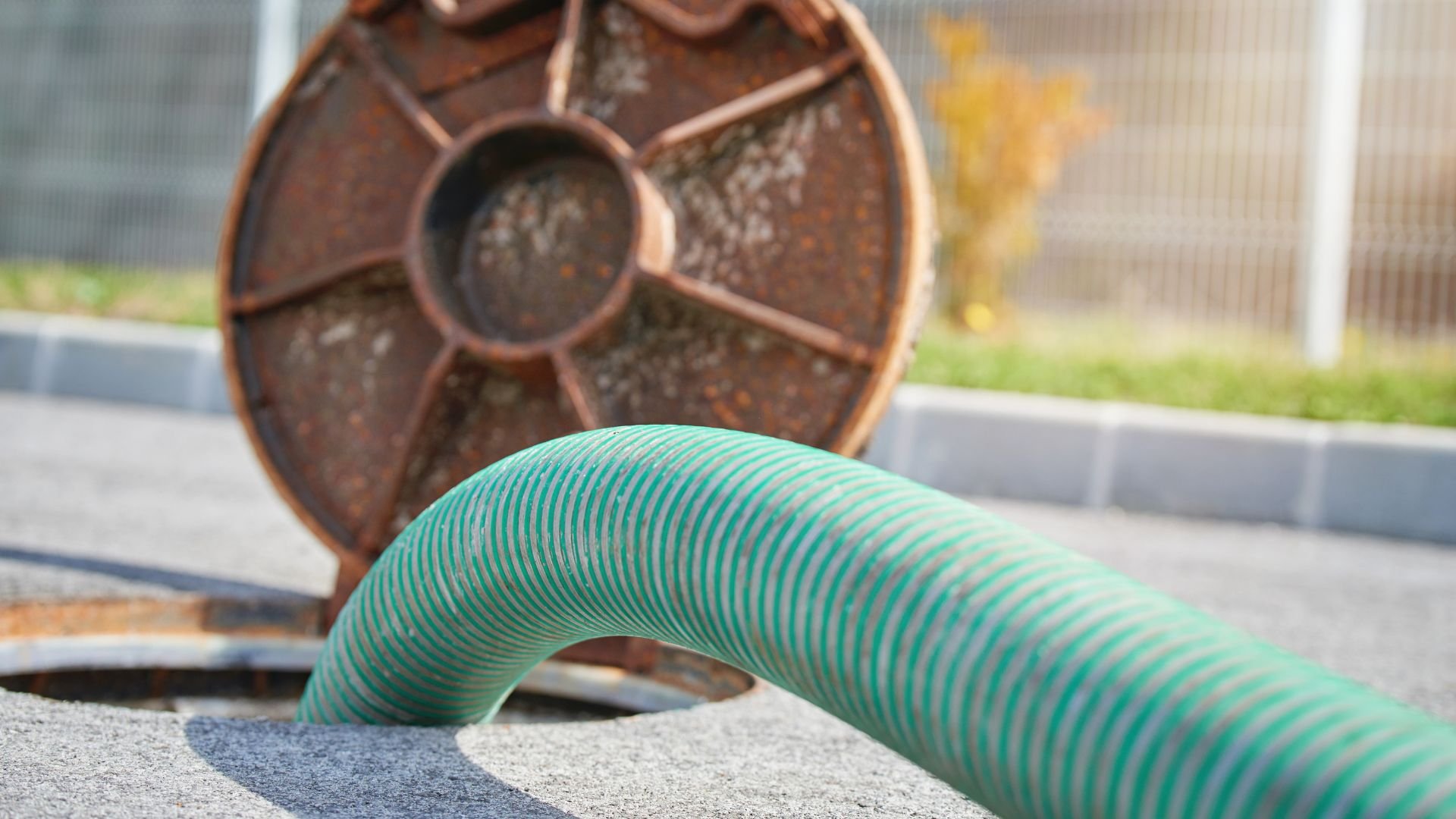 Green garden hose coiled near rusty metal wheel on concrete surface