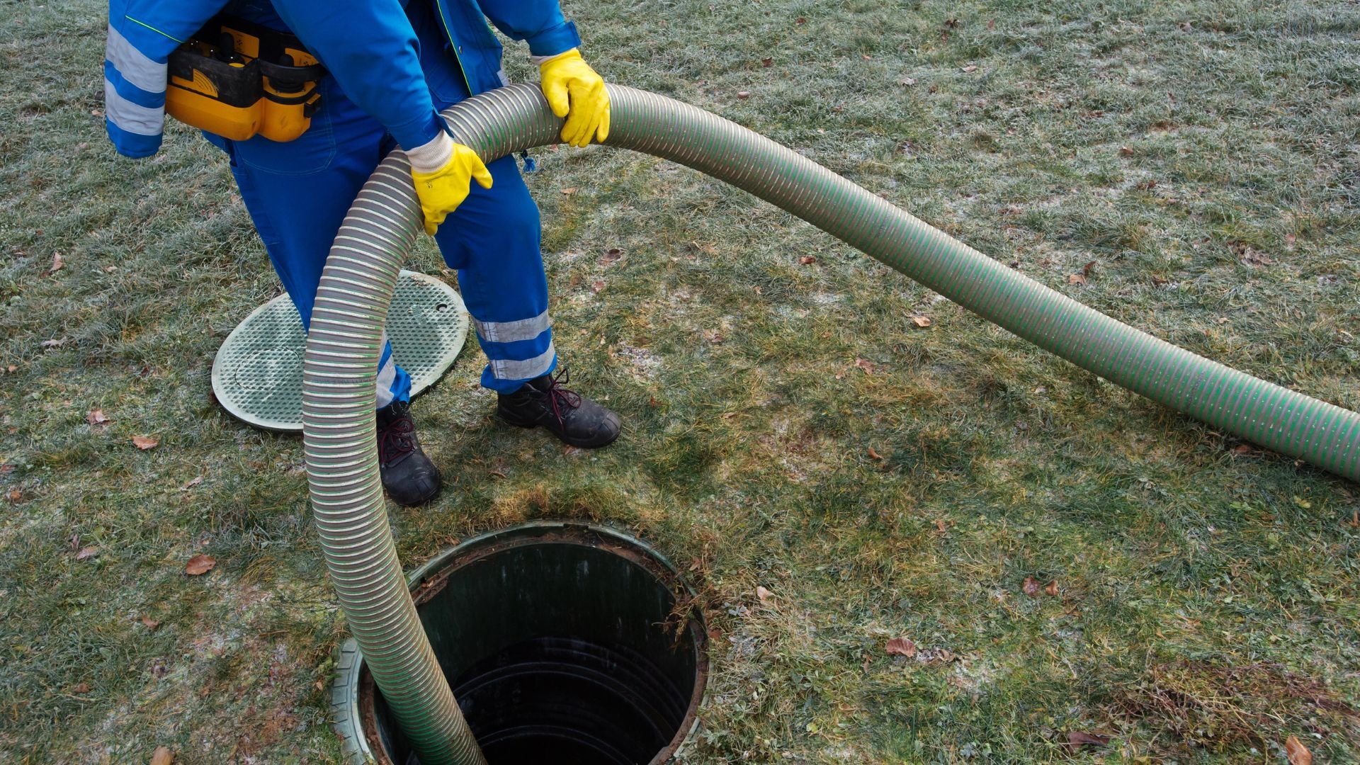Worker with blue uniform and yellow gloves draining sewage through hose