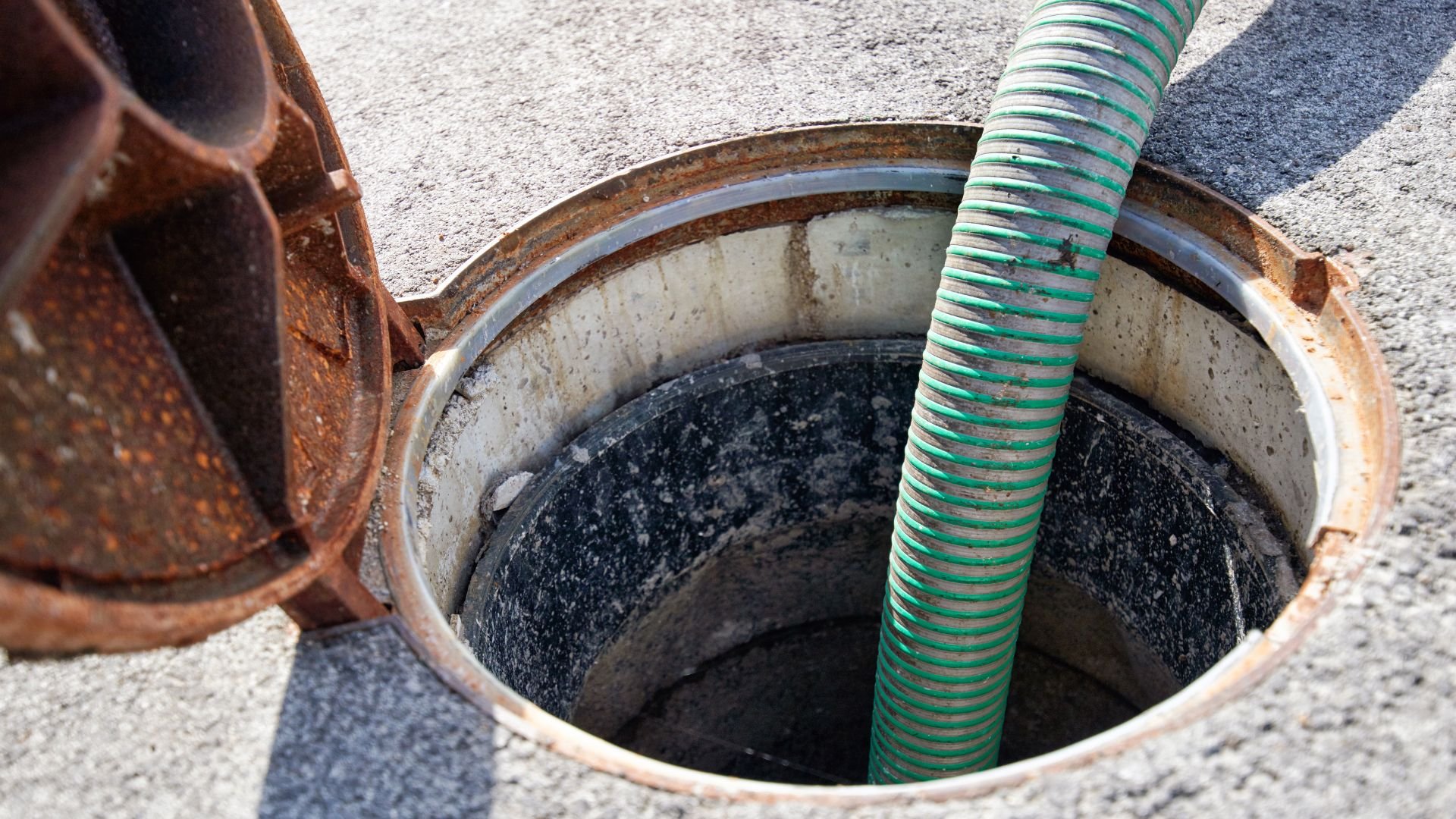 Rusty manhole cover with green corrugated pipe on concrete surface