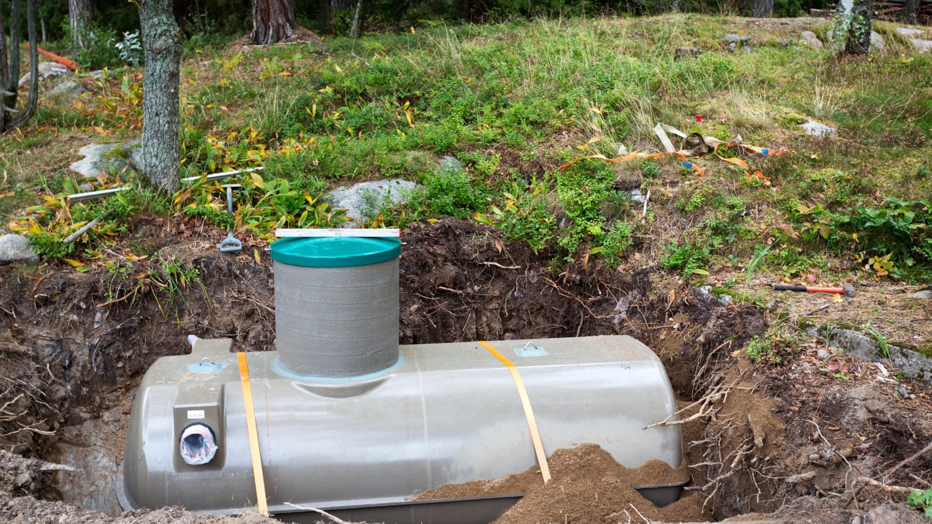 Large underground tank installed in forest clearing with straps and green cap