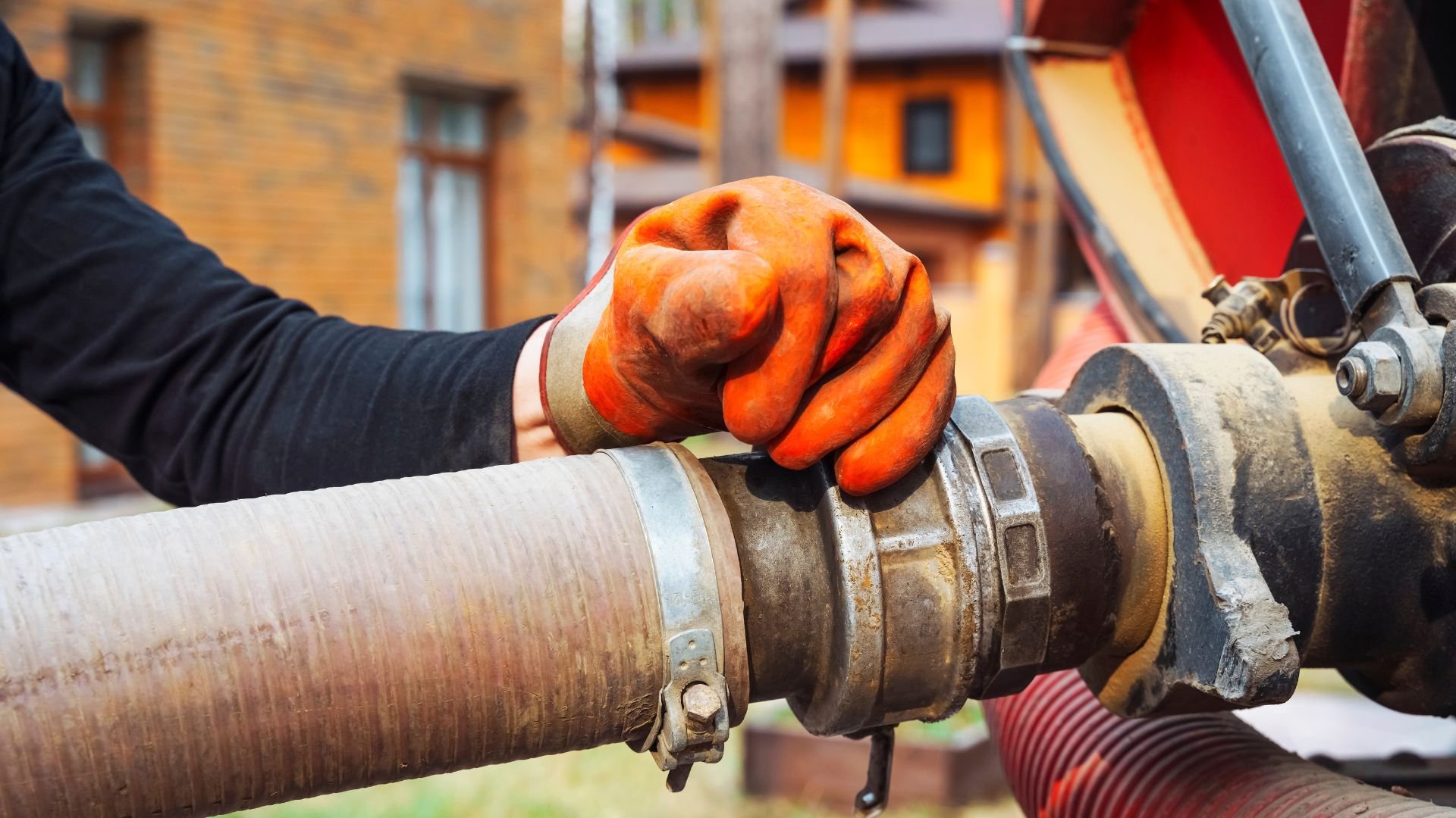 Orange-gloved hand gripping industrial pipe connection outdoors