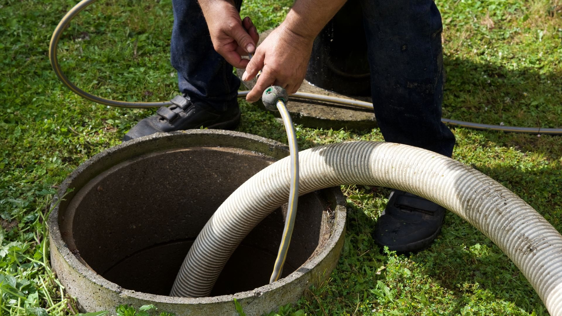 Drain cleaning professional using hose to unclog underground septic tank