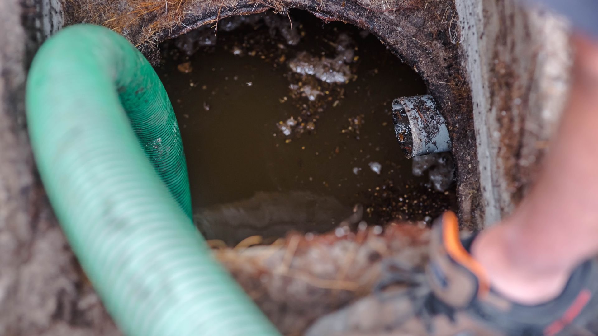 Green flexible pipe near muddy water inside worn concrete drainage structure