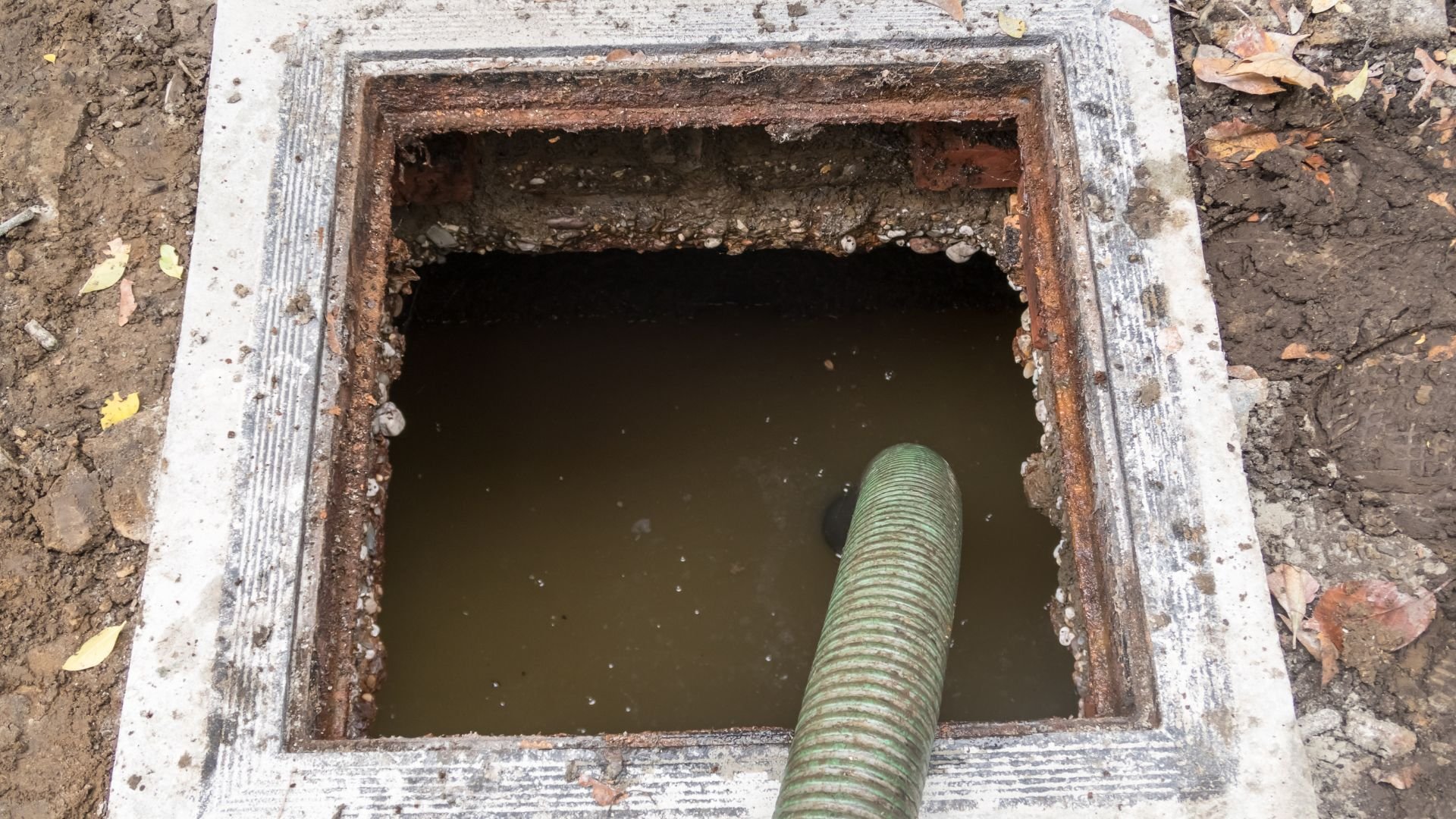 Rusty concrete drainage well with muddy water and green corrugated pipe