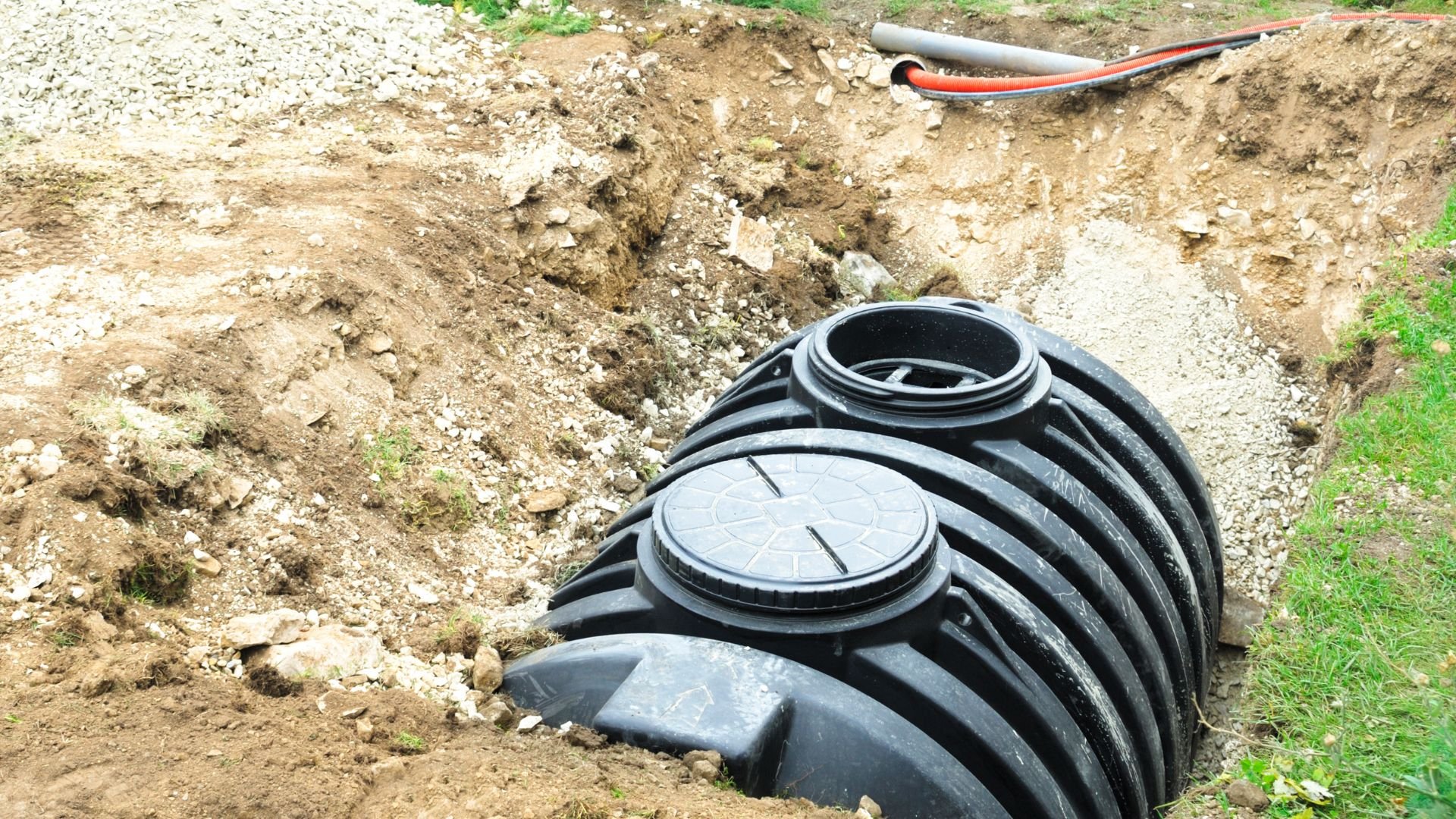 Black plastic septic tank installed in excavated ground with pipes