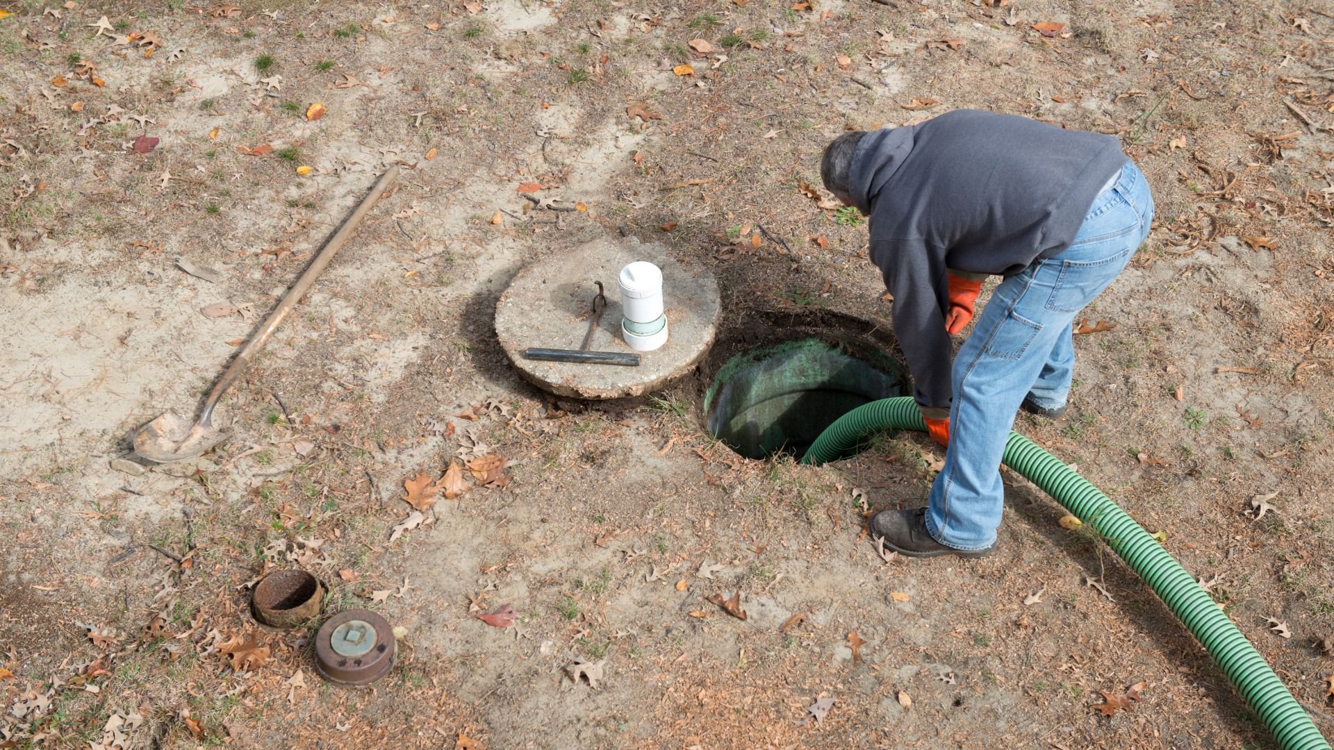 Person inspecting underground utility access point with green drainage hose